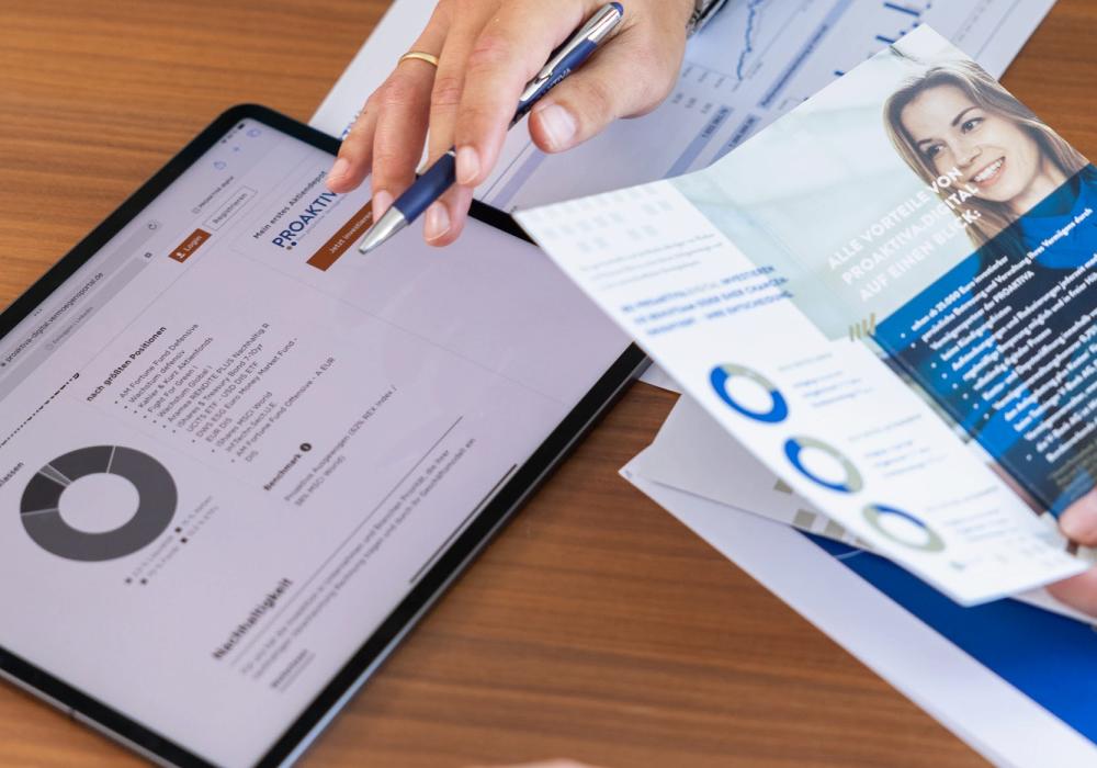 Ein Tablet mit der PROAKTIVA-digital-Webseite, sowie Flyer-Material und Hände, die darauf zeigen